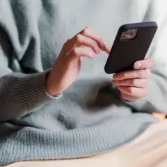 Dłonie w jasnym swetrze trzymają czarny telefon, wykonując skanowanie telefonu.