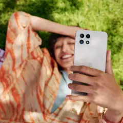 Uśmiechnięta osoba leży na trawie, trzymając telefon. Dowiedz się, jak sprawdzić czas spędzony na telefonie, by cieszyć się chwilą.