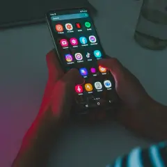Dłonie trzymają smartfon z ikonami aplikacji. Widać Netflix, Spotify, Instagram, TikTok. Bateria szybko się rozładowuje, co widać po intensywnym użytkowaniu.