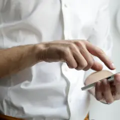 Mężczyzna w białej koszuli dotyka ekranu telefonu, szukając sposobu, jak przenieść SMS z telefonu na telefon.