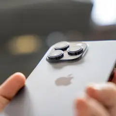 Dłoń trzyma iPhone 14 Pro. Zbliżenie na moduł aparatów i logo Apple. Długi czas pracy baterii to jego atut.