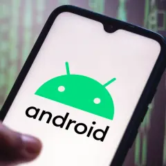 Dłoń trzyma smartfon z logo Android 10. W tle widać zielony, cyfrowy kod.