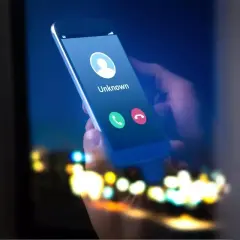 Dłoń trzyma smartfon z ekranem pokazującym przychodzące połączenie od nieznanego numeru. Może to być kod na numer prywatny.