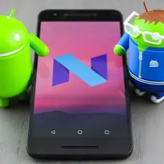 Dwa zielone roboty Android stoją obok smartfona z logo Android 7.0 Nougat na ekranie.