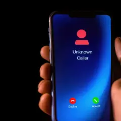 Dłoń trzyma smartfon z ekranem pokazującym "Unknown Caller". Zastanawiasz się, jak zastrzec numer?