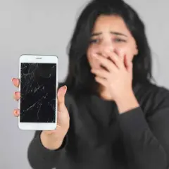 Zrozpaczona kobieta pokazuje pęknięty, czarny ekran w telefonie.