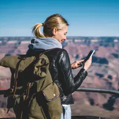 Kobieta z plecakiem w Wielkim Kanionie sprawdza telefon, planując dalszą podróż – roaming krajowy a międzynarodowy.