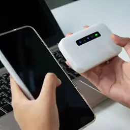 Ręce trzymają smartfon i białe urządzenie mobilne, które tworzy hotspot. To rozwiązanie, gdy potrzebujesz internetu wszędzie.