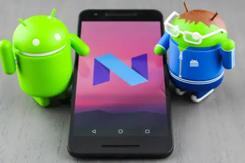 Dwa zielone roboty Android stoją obok smartfona z logo Android 7.0 Nougat na ekranie.