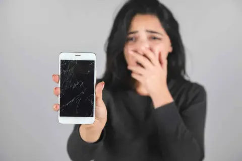 Zrozpaczona kobieta pokazuje pęknięty, czarny ekran w telefonie.