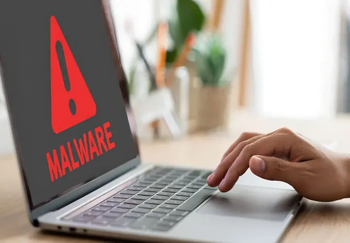 Czerwony wykrzyknik i napis "MALWARE" na ekranie laptopa ostrzegają przed zagrożeniem, takim jak spyware.