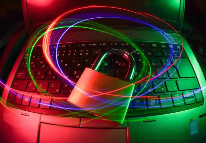 Kłódka na klawiaturze laptopa otoczona kolorowymi światłami. Szukasz darmowy antywirus na laptopa? Zabezpiecz swój sprzęt!