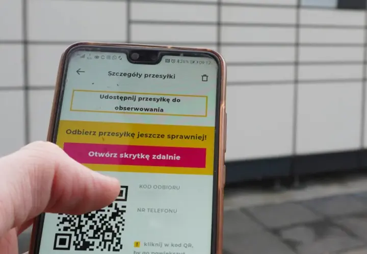 Dłoń trzyma smartfon z aplikacją InPost, wyświetlającą kod QR i opcję otwarcia skrytki.