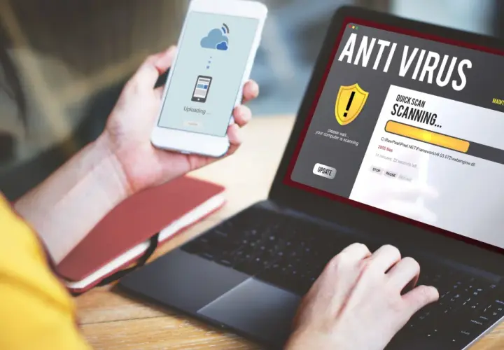 Osoba korzysta z laptopa z programem antywirus free, który skanuje komputer. Na telefonie widnieje komunikat o przesyłaniu danych.