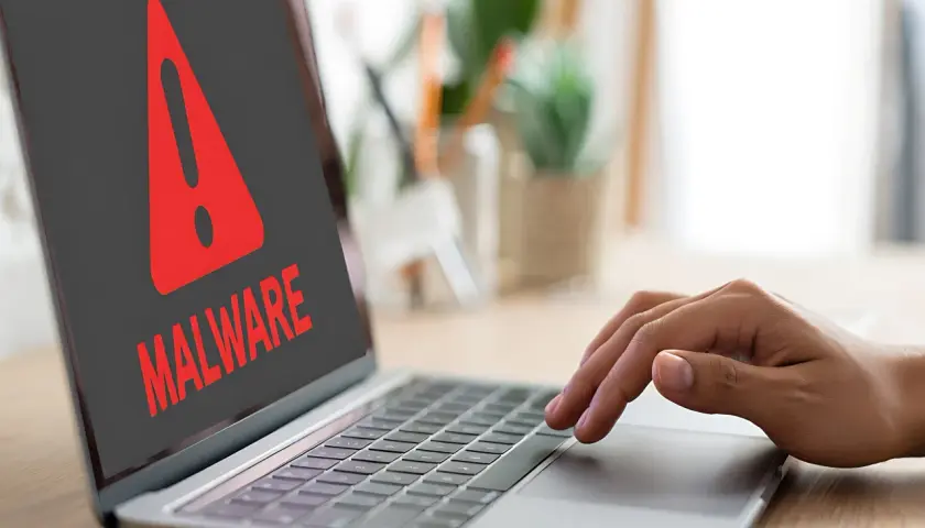Czerwony wykrzyknik i napis "MALWARE" na ekranie laptopa ostrzegają przed zagrożeniem, takim jak spyware.