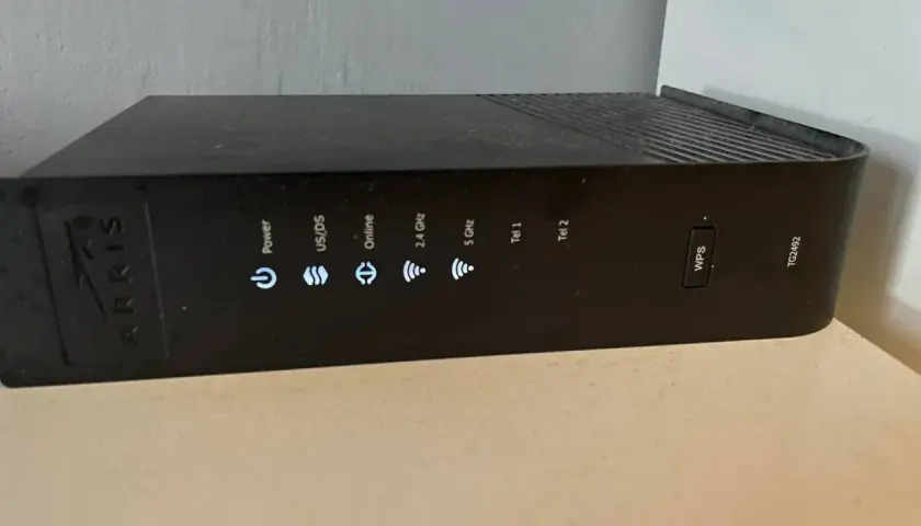 Czarny router Arris z widocznym przyciskiem WPS i wskaźnikami statusu: Power, US/DS, Online, 2.4 GHz, 5 GHz, Tel 1, Tel 2.