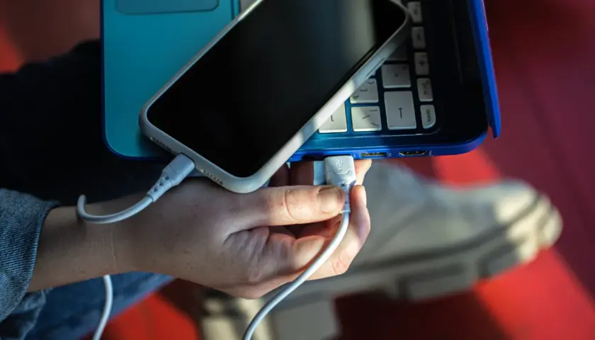 Dłoń podłącza kabel USB telefonu do laptopa, pokazując, jak połączyć telefon z laptopem.