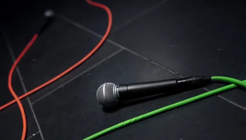Mikrofon Shure leży na czarnej podłodze, otoczony kolorowymi kablami. Chcesz wiedzieć, jak wyczyścić mikrofon w telefonie?