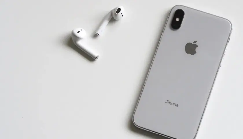 Srebrny iPhone i białe słuchawki AirPods leżą na białym tle. Może rozmówca na iPhonie słabo słychać?
