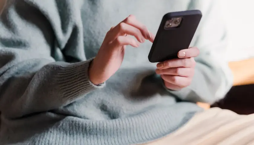 Dłonie w jasnym swetrze trzymają czarny telefon, wykonując skanowanie telefonu.