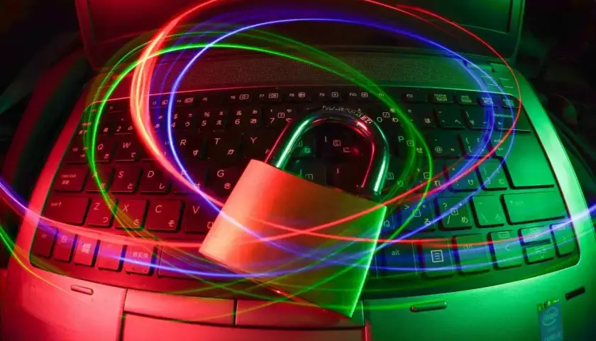 Kłódka na klawiaturze laptopa otoczona kolorowymi światłami. Szukasz darmowy antywirus na laptopa? Zabezpiecz swój sprzęt!