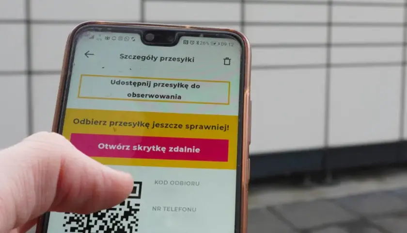 Dłoń trzyma smartfon z aplikacją InPost, wyświetlającą kod QR i opcję otwarcia skrytki.