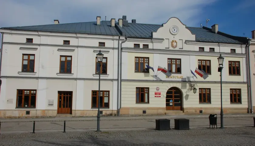 Rektorat w mieście, gdzie kierunkowy 13 wskazuje drogę. Budynek z zegarem i polskimi flagami.