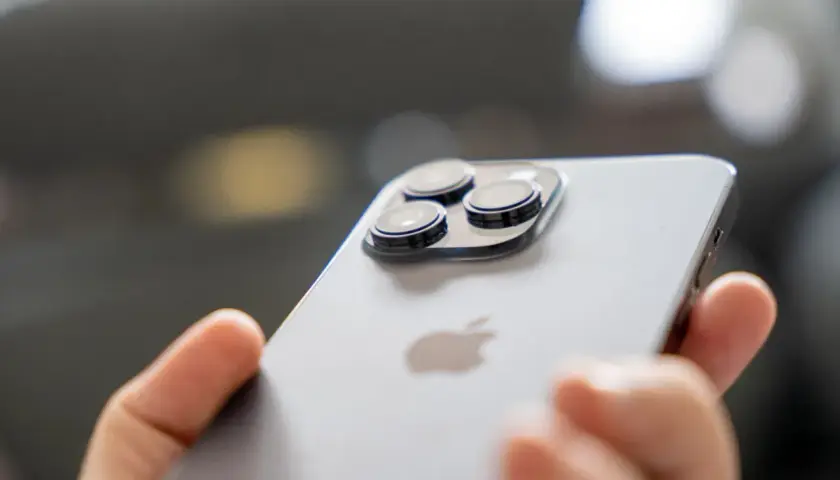 Dłoń trzyma iPhone 14 Pro. Zbliżenie na moduł aparatów i logo Apple. Długi czas pracy baterii to jego atut.