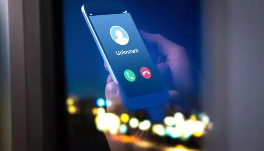 Dłoń trzyma smartfon z ekranem pokazującym przychodzące połączenie od nieznanego numeru. Może to być kod na numer prywatny.