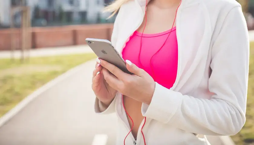 Kobieta w sportowym stroju trzyma iPhone'a, słuchając muzyki. Chcesz wiedzieć, jak włączyć Siri?