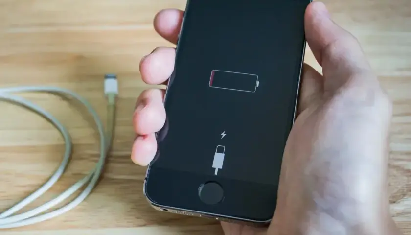 Dłoń trzyma telefon, na którego ekranie widać ikonę pustej baterii i symbol ładowania. Telefon się nie ładuje.