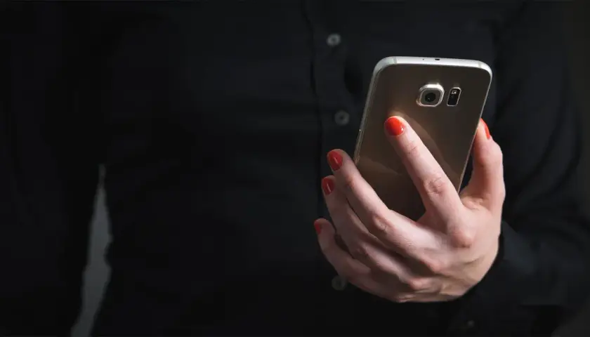 Dłoń z czerwonymi paznokciami trzyma telefon, szukając informacji, jak zablokować SMS premium.