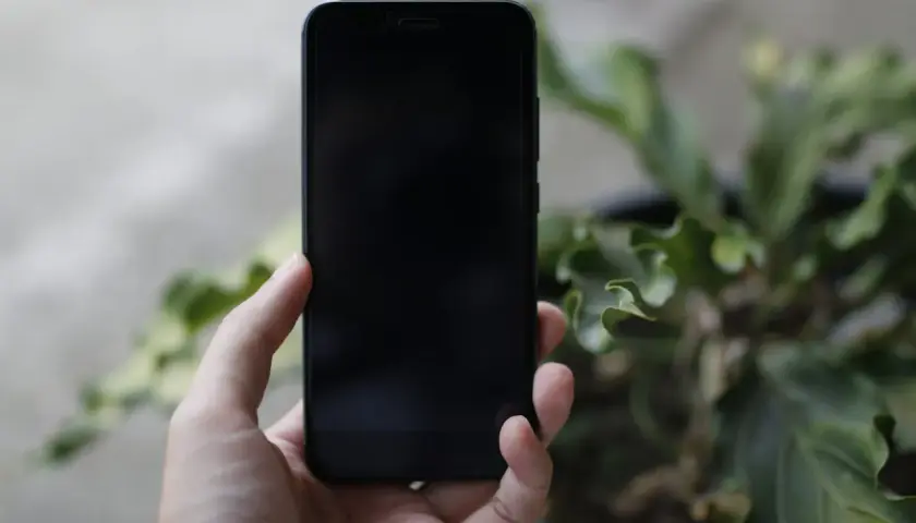 Dłoń trzyma czarny iPhone. Zastanawiasz się, jak wyłączyć iPhone bez dotyku?