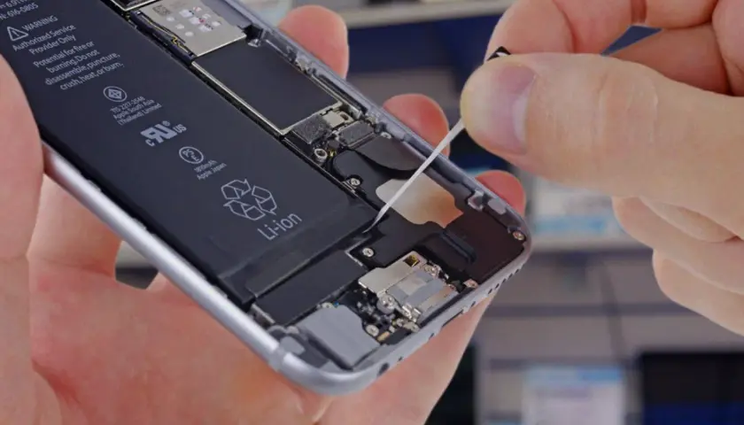 Wymiana baterii w iPhone. Dłoń wyciąga taśmę z wnętrza telefonu, odsłaniając baterię Li-ion.