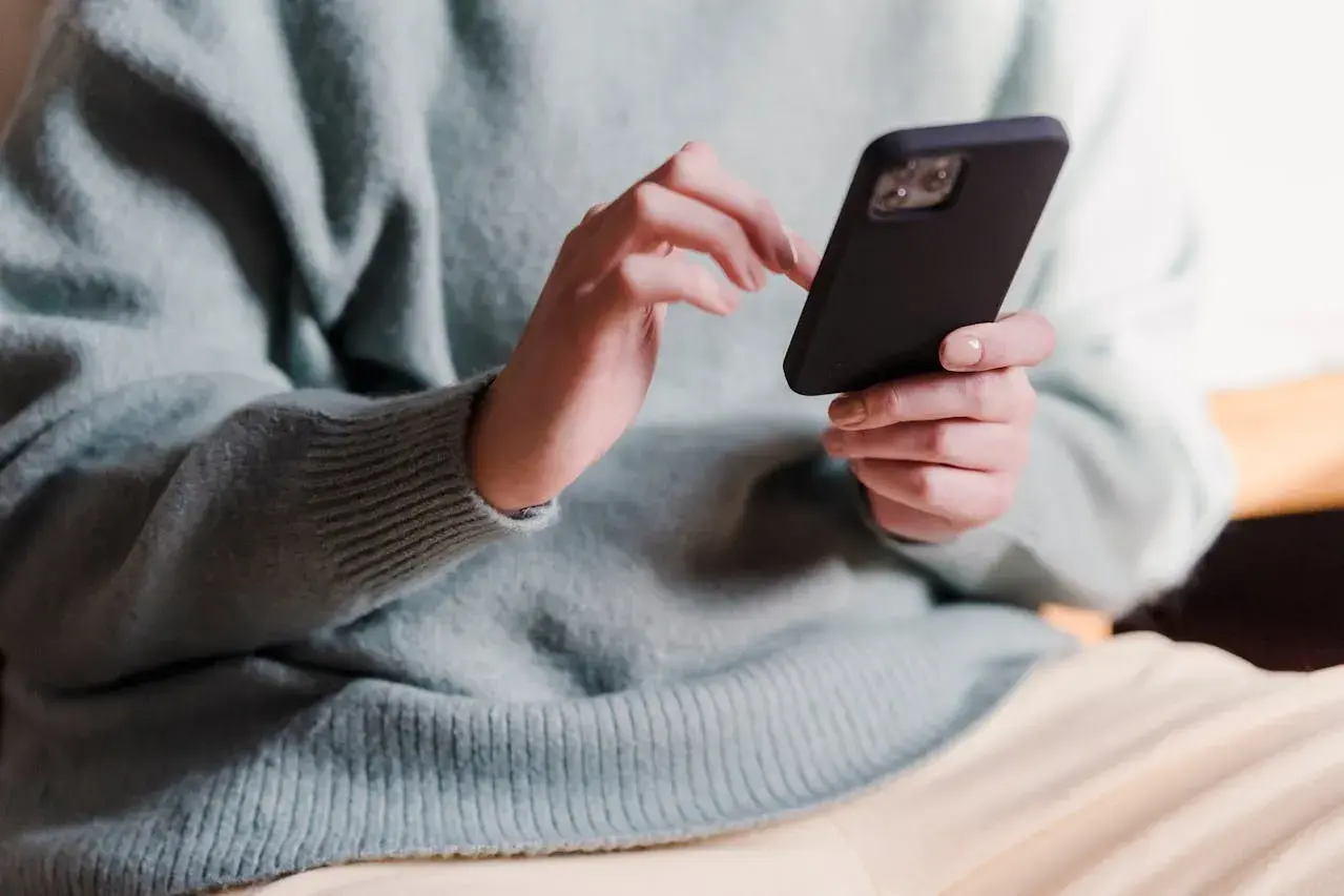 Dłonie w jasnym swetrze trzymają czarny telefon, wykonując skanowanie telefonu.