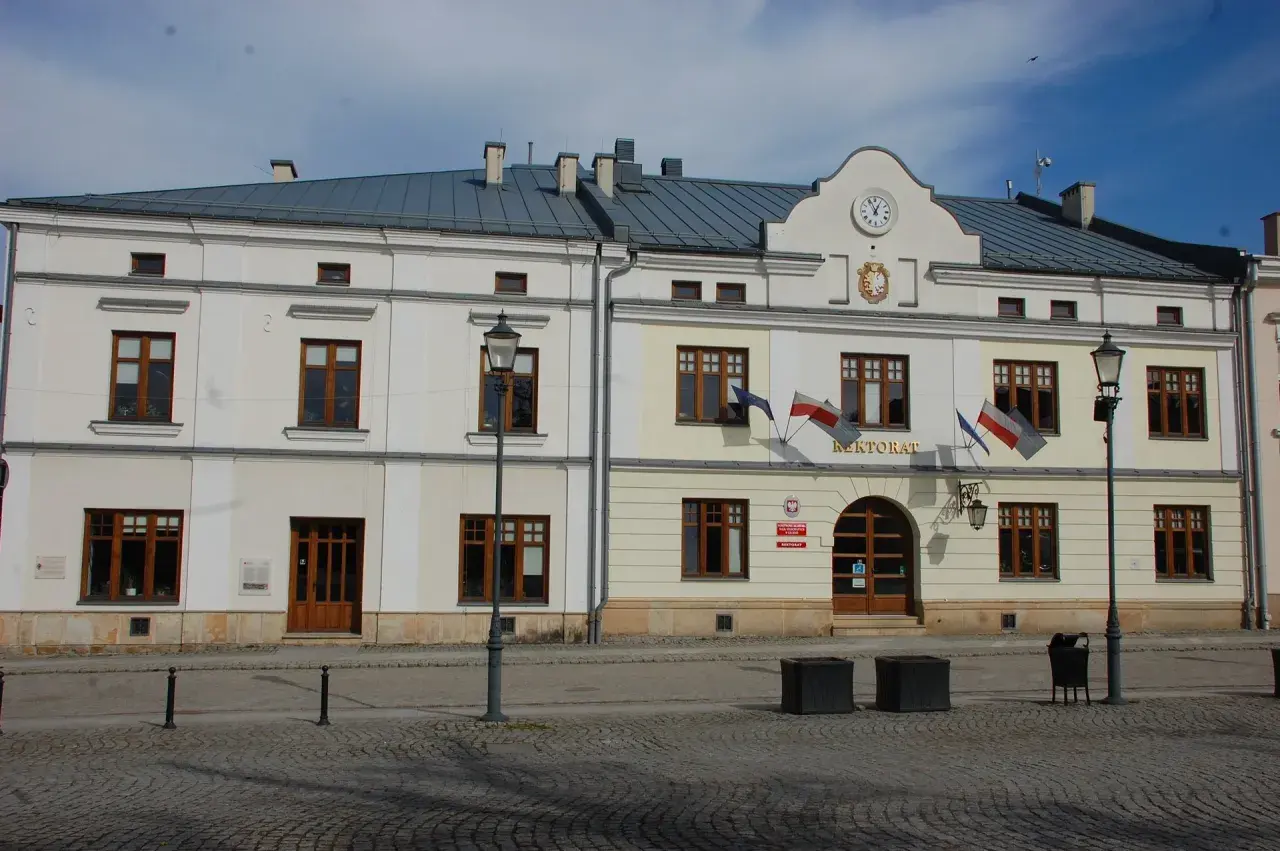 Rektorat w mieście, gdzie kierunkowy 13 wskazuje drogę. Budynek z zegarem i polskimi flagami.