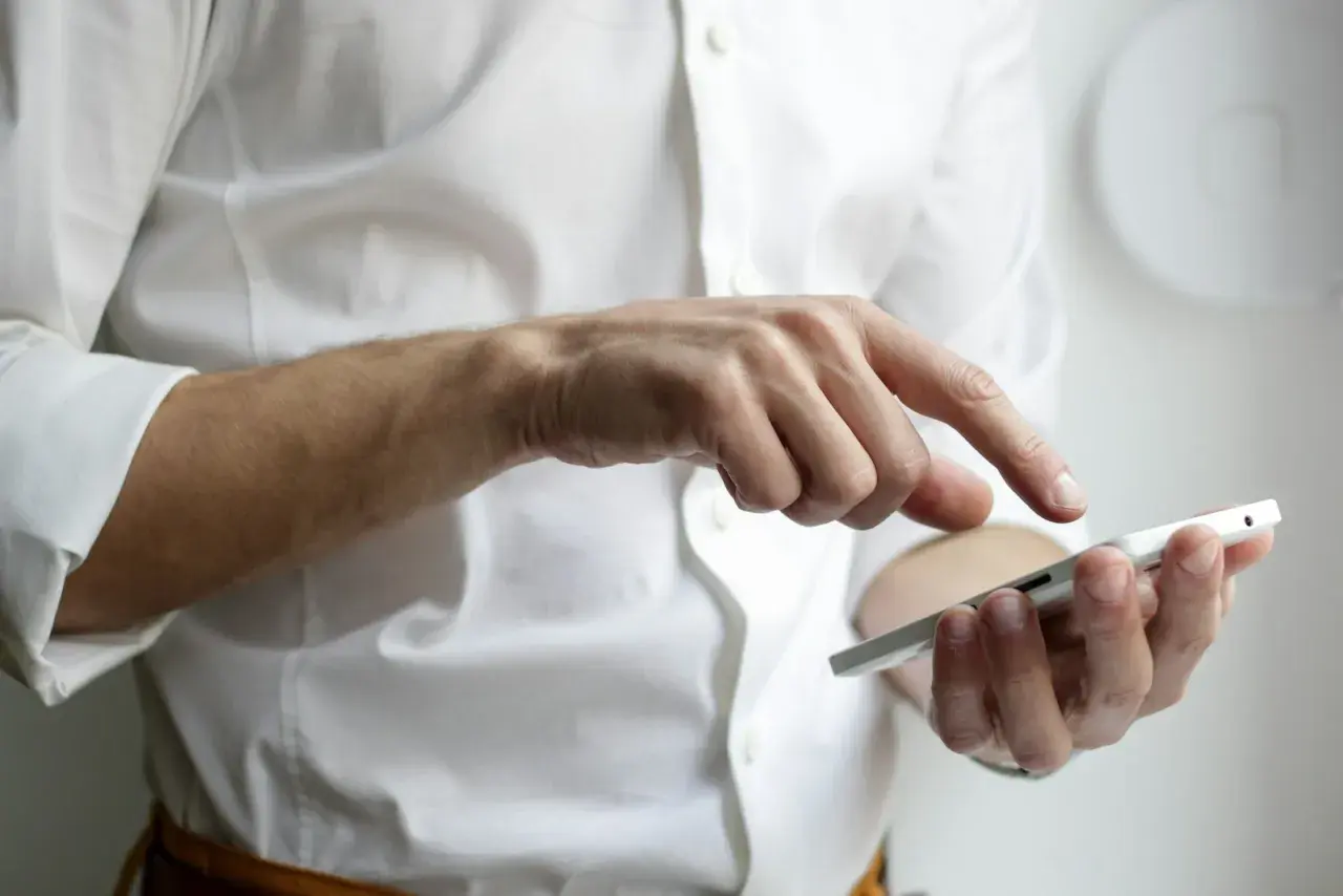 Mężczyzna w białej koszuli dotyka ekranu telefonu, szukając sposobu, jak przenieść SMS z telefonu na telefon.