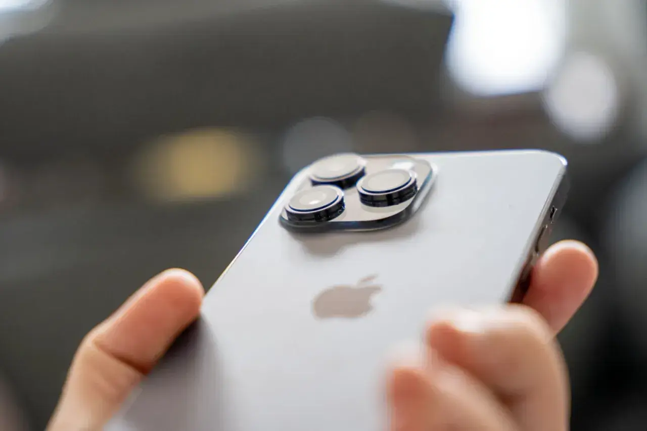 Dłoń trzyma iPhone 14 Pro. Zbliżenie na moduł aparatów i logo Apple. Długi czas pracy baterii to jego atut.