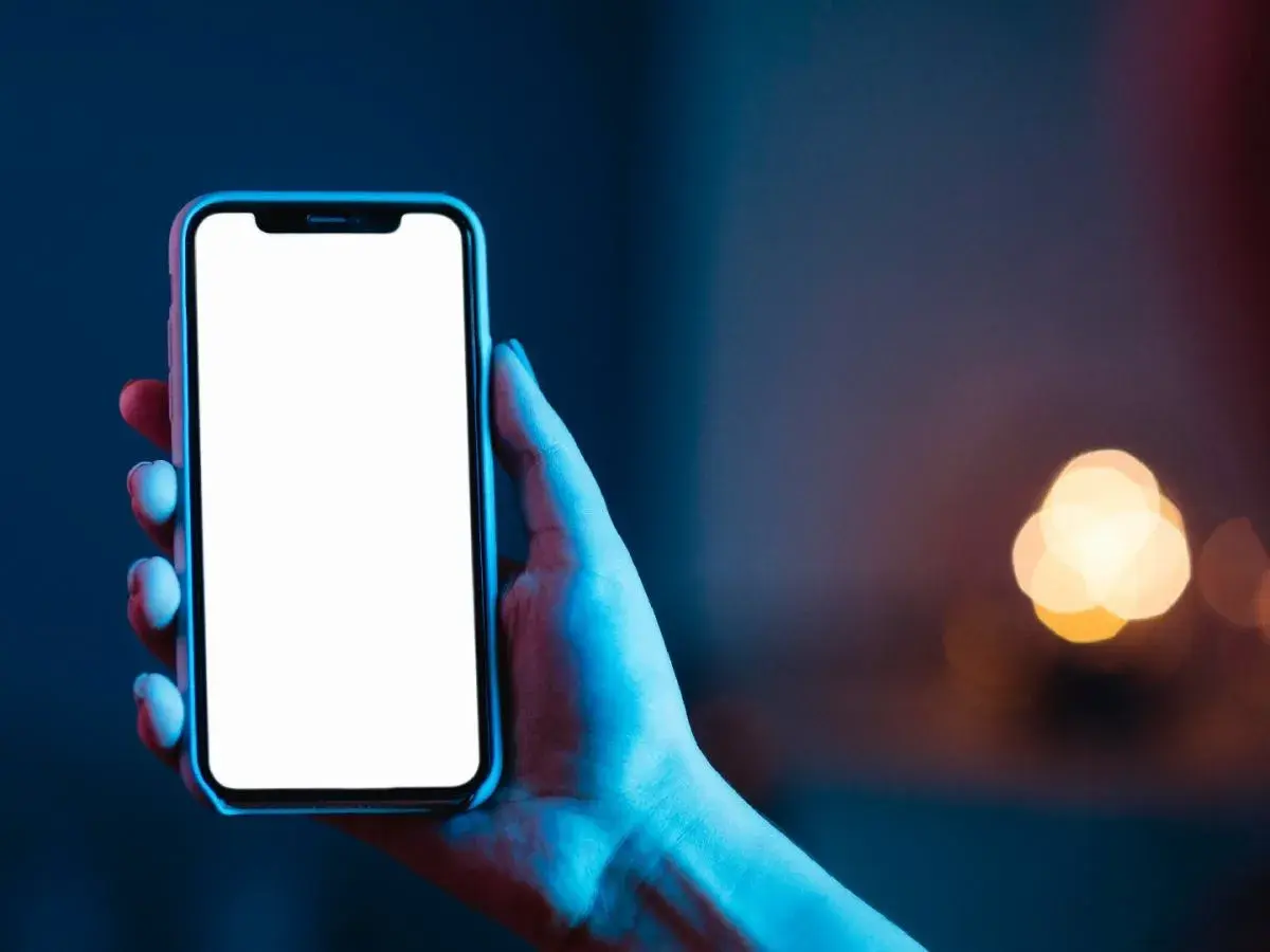 Dłoń trzyma smartfon z pustym ekranem **AMOLED**, otoczony niebieskim i czerwonym światłem.