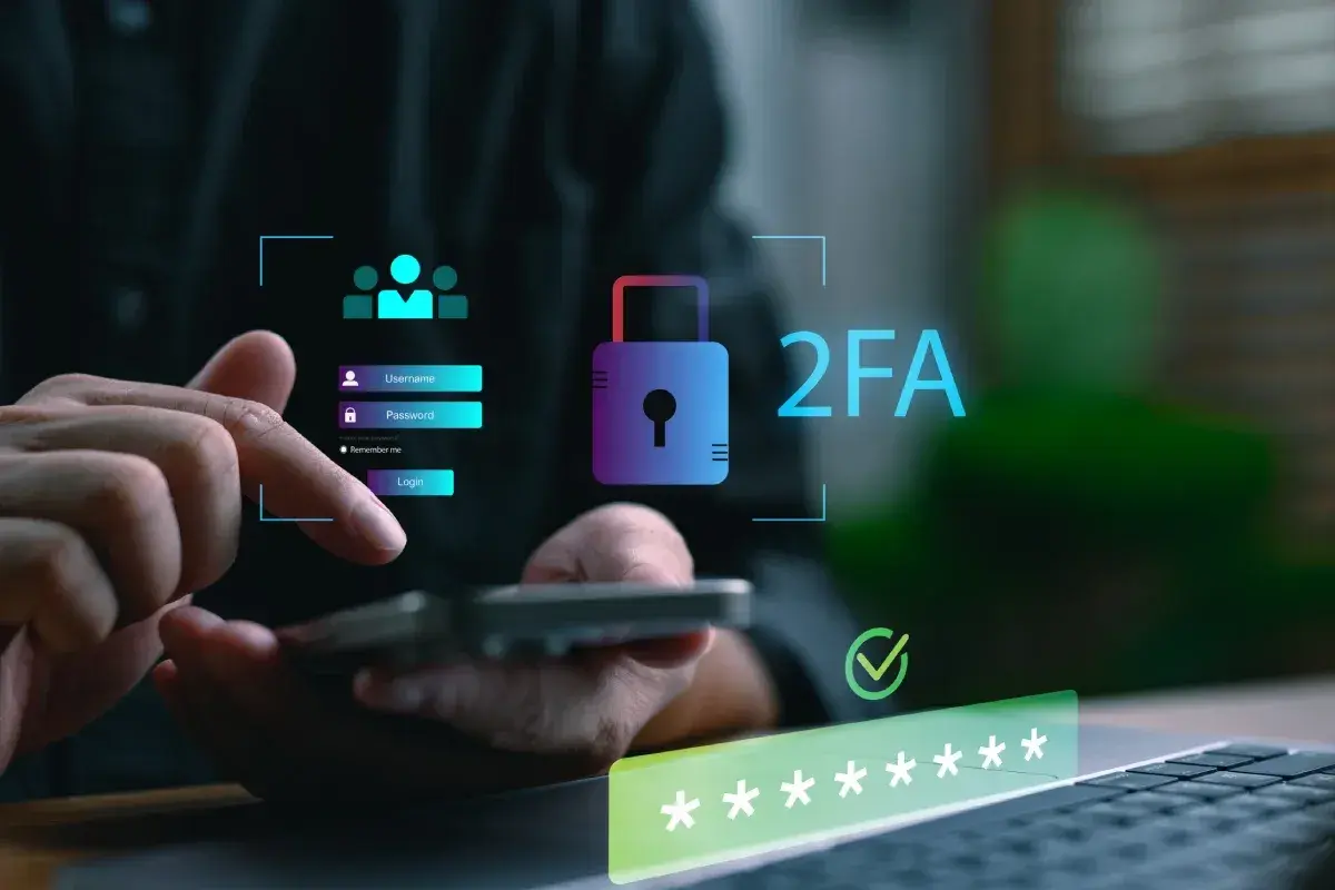 Dłoń wpisuje dane logowania na smartfonie, obok widnieje ikona kłódki i napis 2FA co to, symbolizujące podwójne uwierzytelnianie.