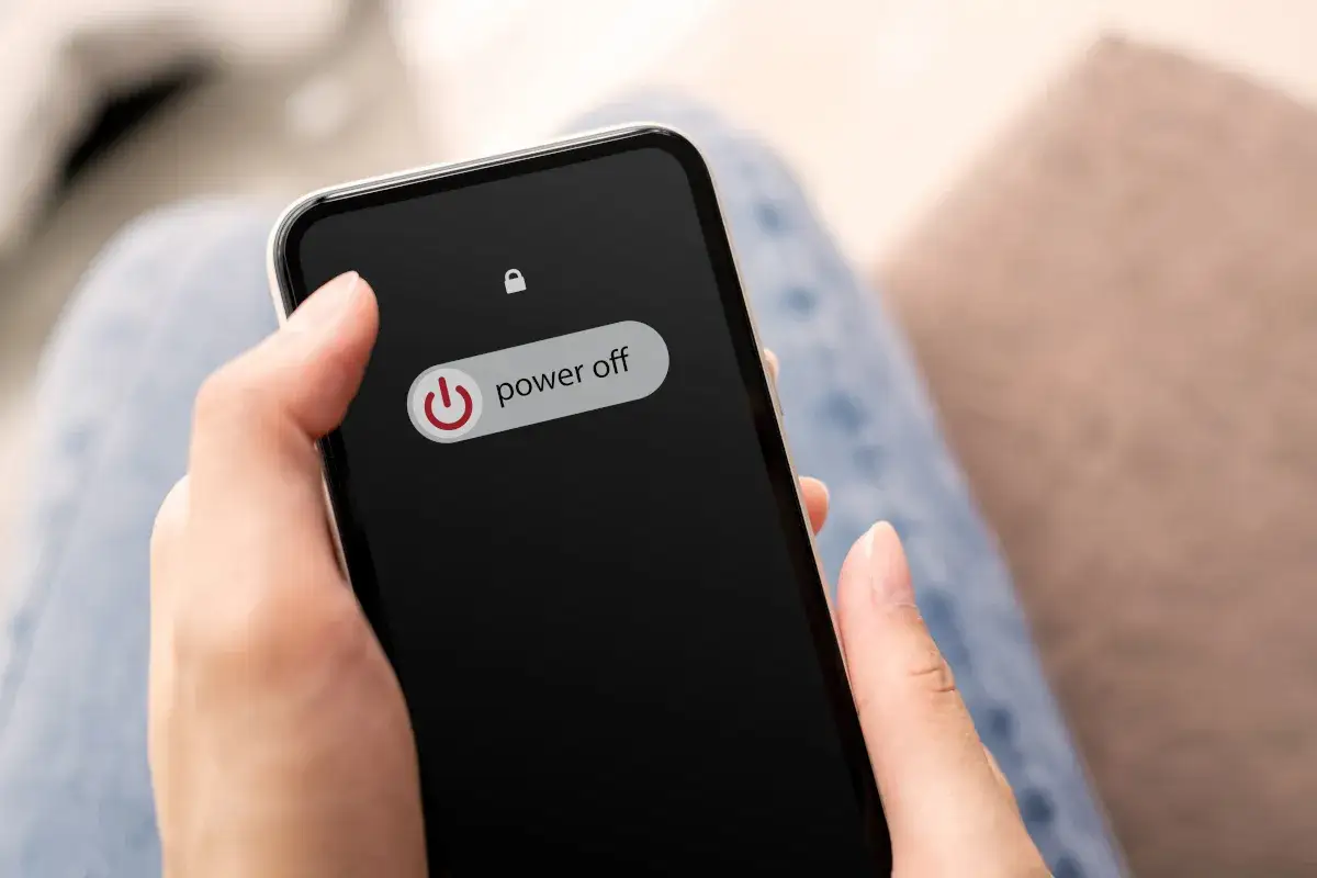 Dłoń trzyma telefon z widocznym przyciskiem