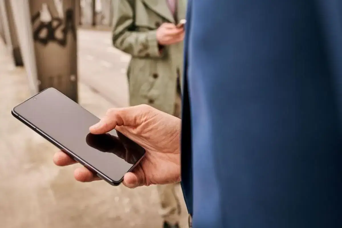 Dłoń trzyma smartfon z czarnym ekranem w telefonie, czekając na wiadomość.