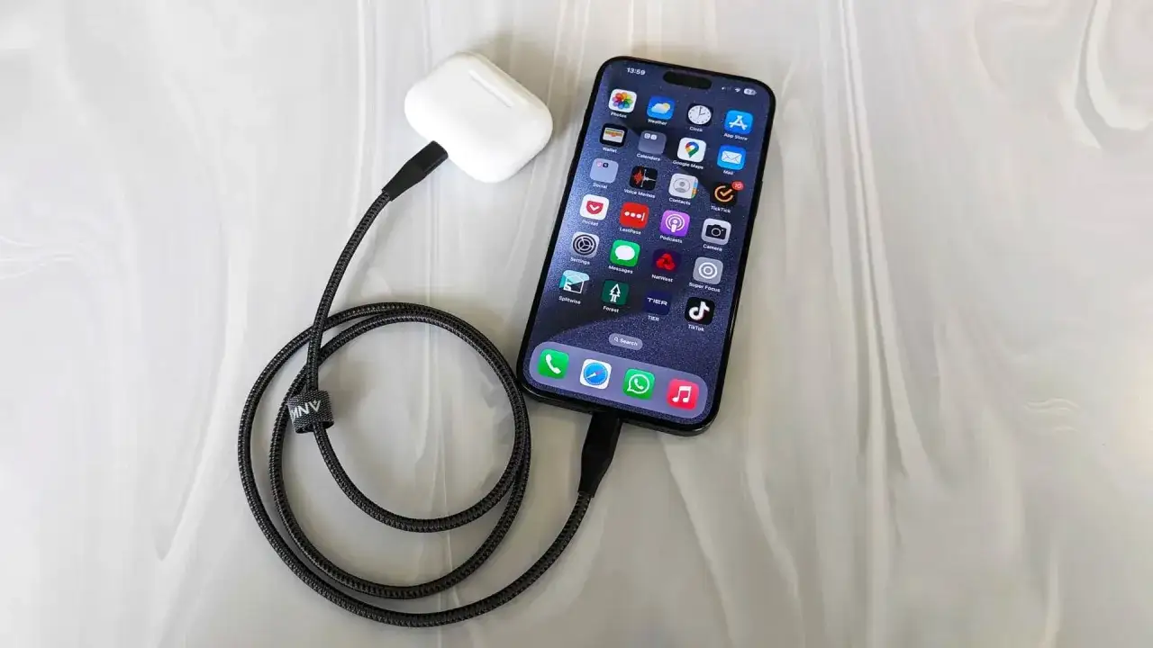 iPhone z podłączonymi słuchawkami ładuje się zwrotnie, pokazując ekran główny z ikonami aplikacji.