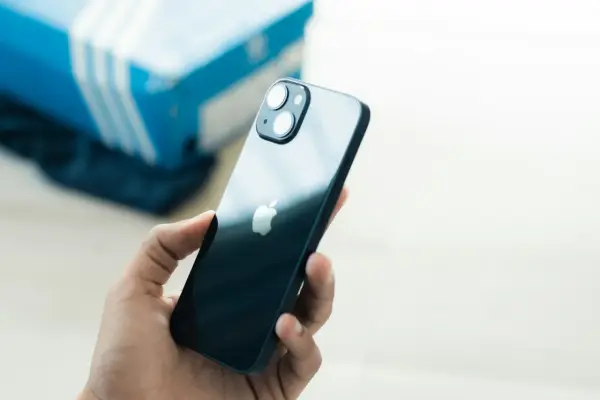 Dłoń trzyma ciemny iPhone 13. Czy iPhone 13 jest wodoszczelny? W tle niebieskie pudełko.
